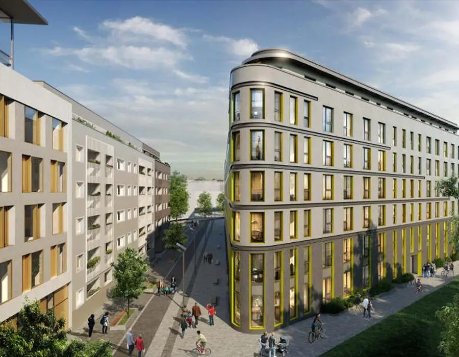 Modernes Eckgebäude an einer begrünten Stadtstraße mit Fußgängern und Radfahrern.