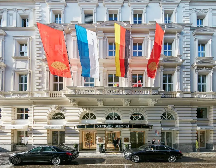 Hotelfassade mit großen Fahnen über dem Haupteingang und parkenden Autos davor.